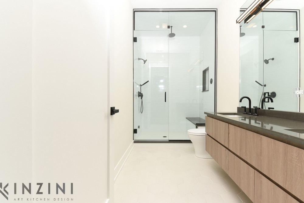 A modern bathroom with a glass-enclosed shower, a toilet, and a dark countertop with wood cabinets underneath. The room features sleek black fixtures and minimalist design elements.