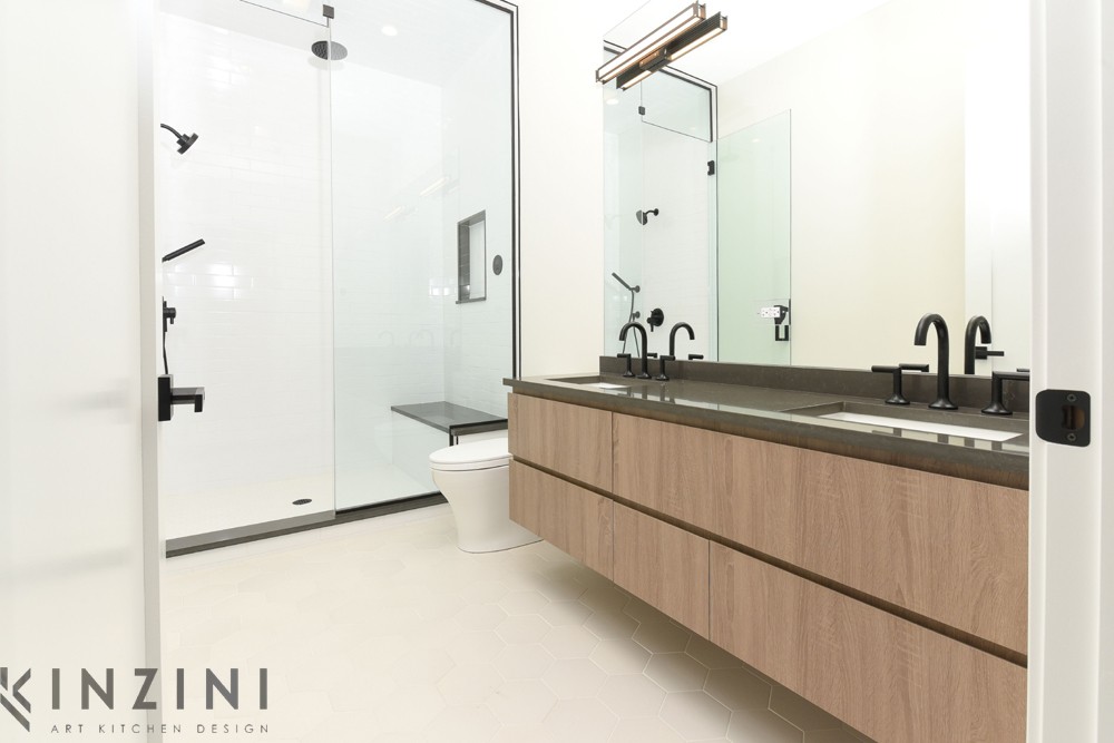 A modern bathroom with a glass-enclosed shower, a toilet, and a dark countertop with wood cabinets underneath. The room features sleek black fixtures and minimalist design elements.